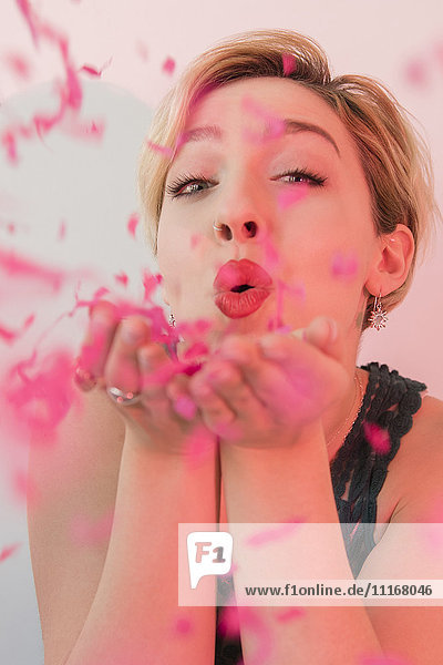 Caucasian woman blowing pink confetti