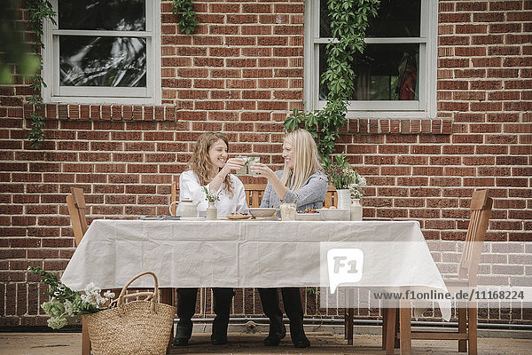 Zwei Frauen sitzen vor einem Haus und nehmen eine Mahlzeit ein.
