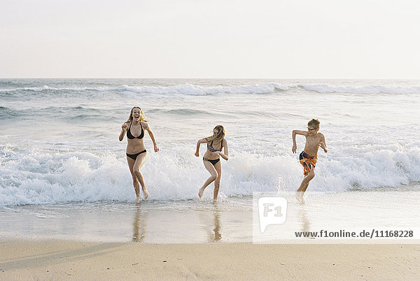 Drei Kinder spielen an einem Sandstrand am Meer.