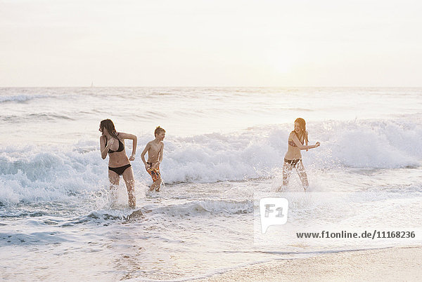 Three children playing on a sandy beach by the ocean.