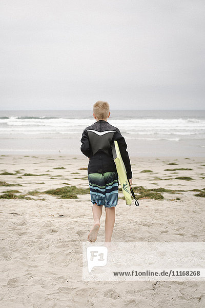 Rear view of a boy carrying a bodyboard  walking into the ocean.