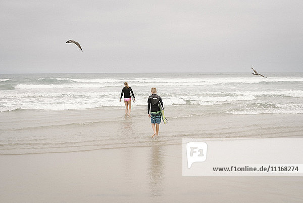 Rückansicht eines Jungen und eines Mädchens  die Bodyboards tragen und in den Ozean gehen.