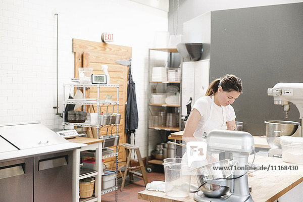 Frau mit weißer Schürze  die an einem Arbeitstresen in einer Bäckerei steht.