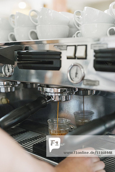 Nahaufnahme eines Mannes  der vor einer Espressomaschine steht  frischer Espresso läuft in eine Tasse.