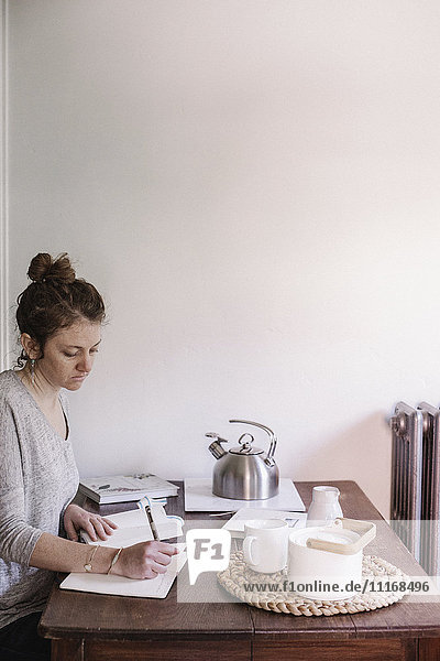Woman sitting at a table in her apartment  writing in a diary  morning routine.