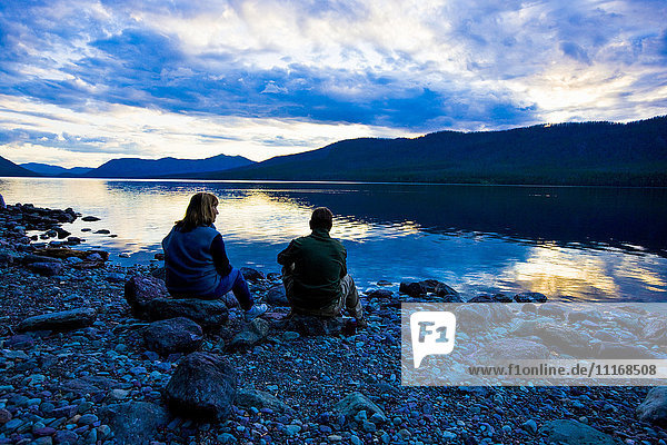 Kaukasisches Paar sitzt bei Sonnenuntergang auf Felsen am See