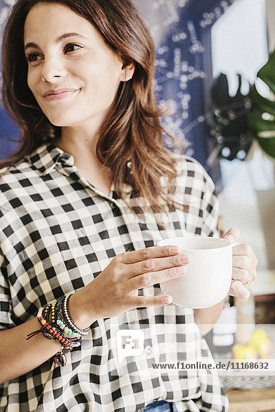 Woman with long brown hair  wearing a chequered shirt  holding a mug.