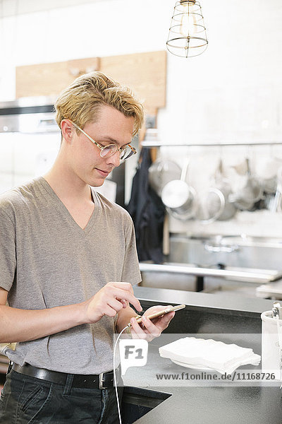 Young blond man wearing glasses  standing in a coffee shop  using his cell phone.