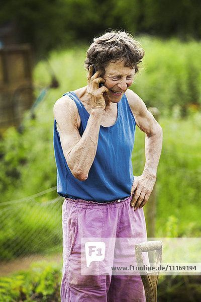 Eine Frau telefoniert auf einem Bauernhof mit einer Schaufel am Bein.