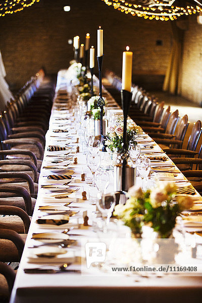 Ein Hochzeitsort  der für eine Party dekoriert ist  mit Lichterketten und einem langen gedeckten Tisch für das Abendessen.