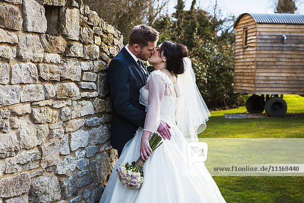 Eine Braut und ein Bräutigam  die sich an ihrem Hochzeitstag küssen und in einem Garten stehen.