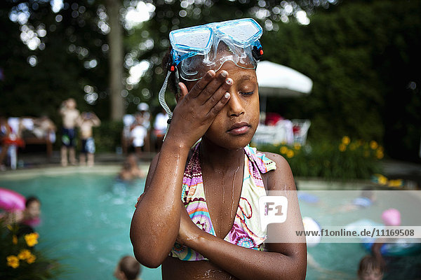Porträt eines jungen Mädchens mit Schwimmbrille und Bikini  das an einem Swimmingpool steht.