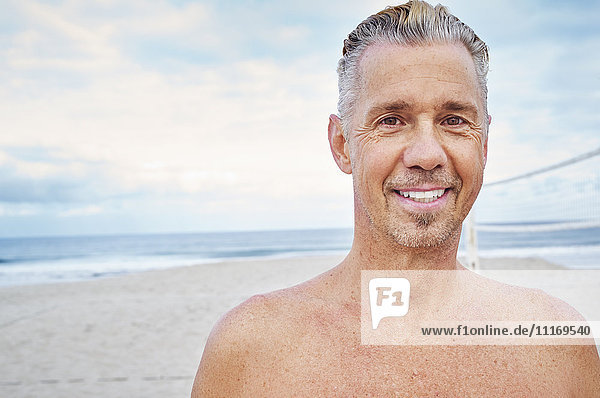 Mature man standing on a beach  smiling at camera.