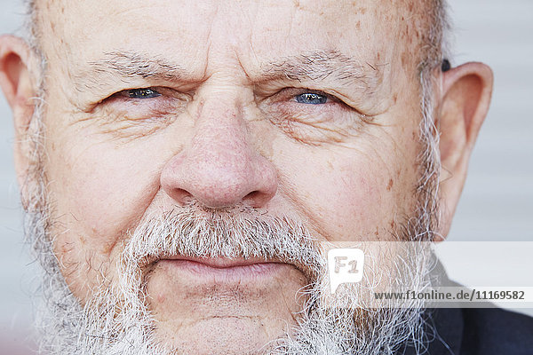 Porträt eines älteren Mannes mit grauem Bart,  der in die Kamera schaut.