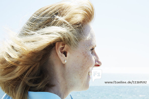 Profil einer blonden,  reifen Frau,  die am Meer steht.