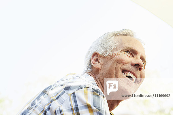 Lächelnder älterer Mann mit grauen Haaren sitzt im Freien.