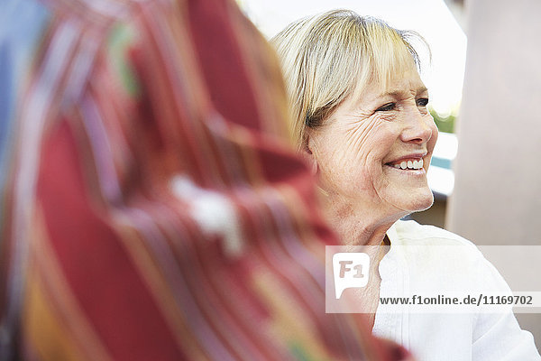 Lächelnde ältere Frau mit blonden Haaren sitzt im Freien.