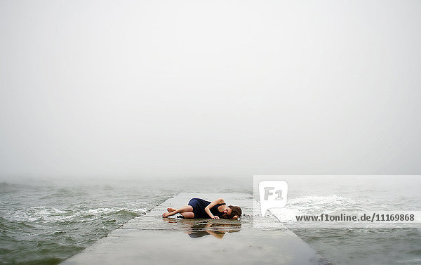 Caucasian woman laying on dock in ocean waves