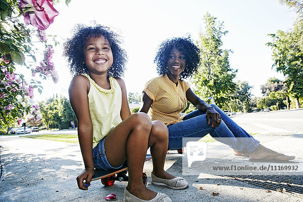 Mutter und Tochter sitzen auf einem Skateboard auf dem Gehweg