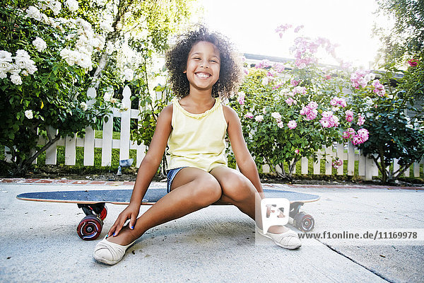 Lächelndes Mixed Race Mädchen auf Skateboard sitzend