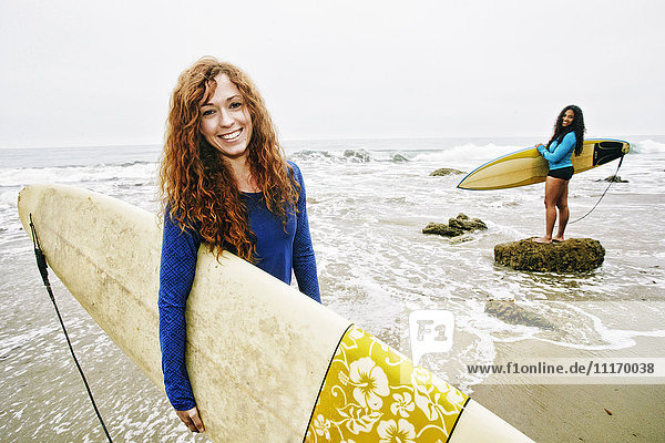 Lächelnde Frauen mit Surfbrettern am Strand