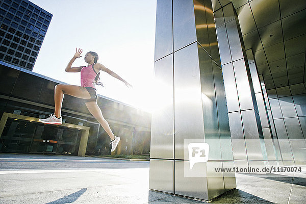 Black woman running and jumping on city sidewalk