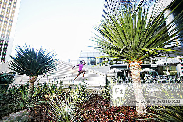 Black woman running and jumping on sidewalk near trees