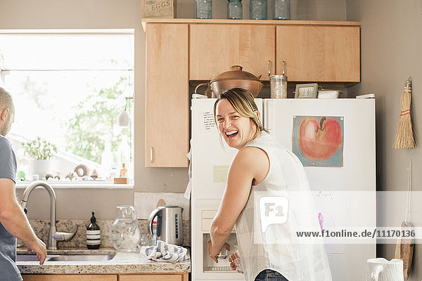 Lächelnde blonde Frau  die an einem Kühlschrank in einer Küche steht.