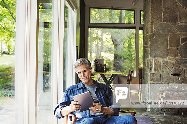 Ein am Fenster sitzender Mann liest mit einem digitalen Tablett.