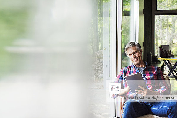 Ein am Fenster sitzender Mann liest mit einem digitalen Tablett. Unscharfer Vordergrund.