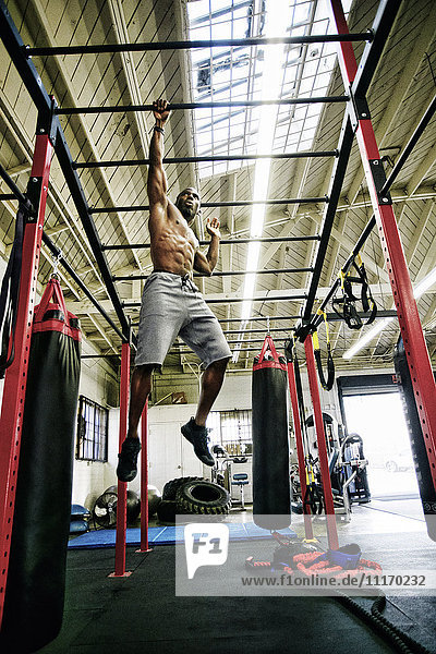 Black man hanging from bars in gymnasium