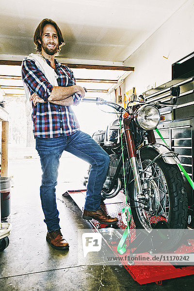 Kaukasischer Mann posiert mit Motorrad in Garage