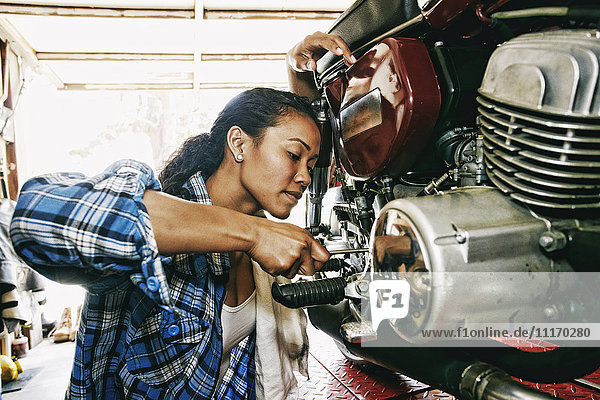 Gemischtrassige Frau repariert Motorrad in Garage