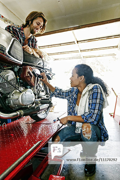 Mann beobachtet Frau bei der Reparatur eines Motorrads in der Garage