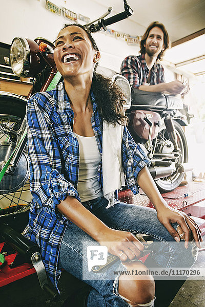 Laughing man and woman repairing motorcycle in garage