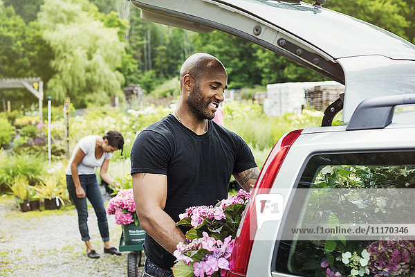 Car parked at a garden centre  a man loading flowers into the boot.