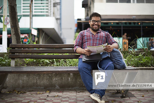 Hispanic man sitting on bench reading brochure