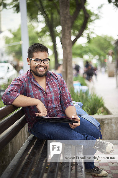 Smiling Hispanic man sitting on bench reading brochure