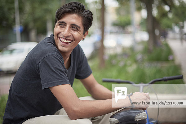 Laughing Hispanic man sitting with bicycle