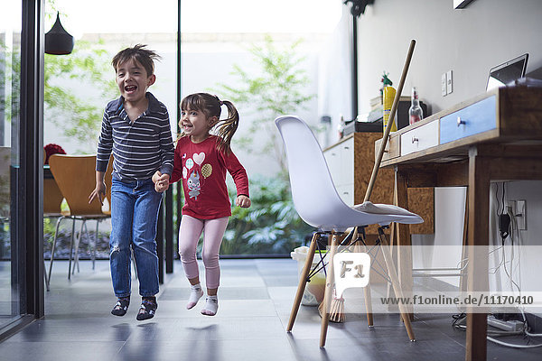 Hispanic brother and sister holding hands and jumping