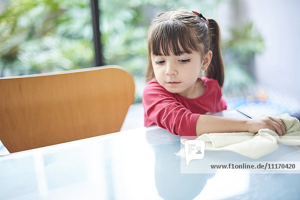 Hispanic girl cleaning table with towel