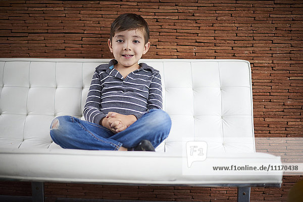 Hispanic boy sitting cross-legged on sofa