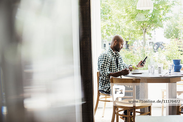 Man wearing a checked shirt sitting in a cafe  using his mobile phone.