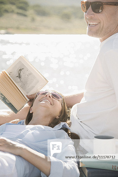 Mann und Frau liegen auf einem Steg und lesen ein Buch.