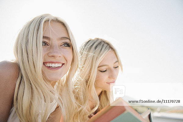 Two blond sisters lying on a jetty  reading a book.