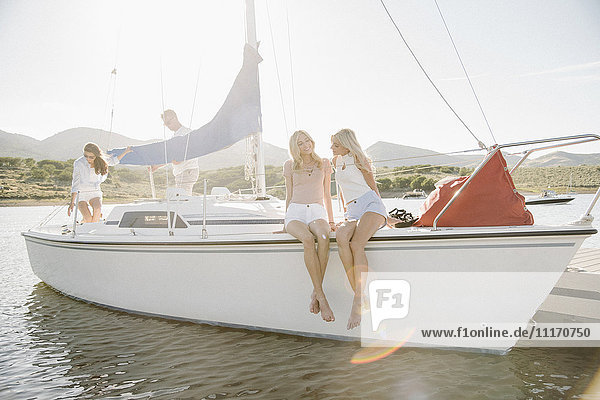 Two blond sisters sitting on a sail boat.