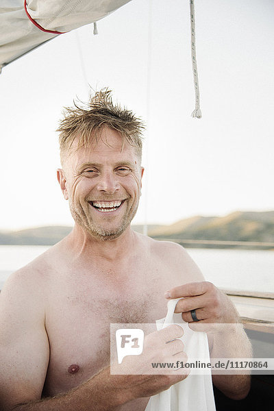 Smiling shirtless man standing on sail boat.