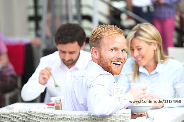 Portrait of happy businessman sitting with colleagues at outdoor restaurant