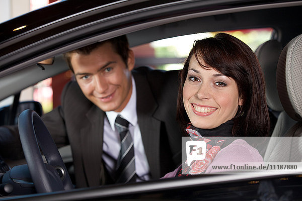 Portrait of young couple sitting in a new car at showroom
