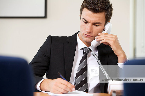 Businessman conversing on landline phone while writing on paper